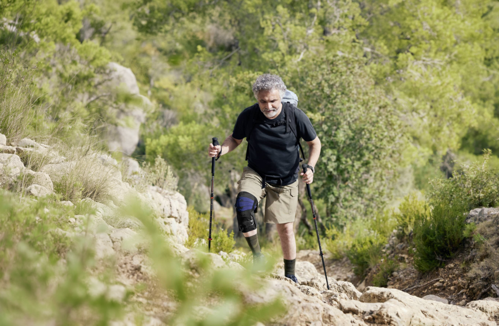 Mann in der Natur wandert mit einer Orthese am Knie.